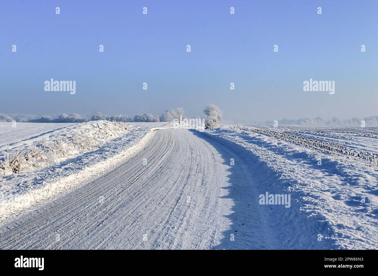 Vue sur une route de campagne enneigée en hiver avec soleil et ciel bleu Banque D'Images