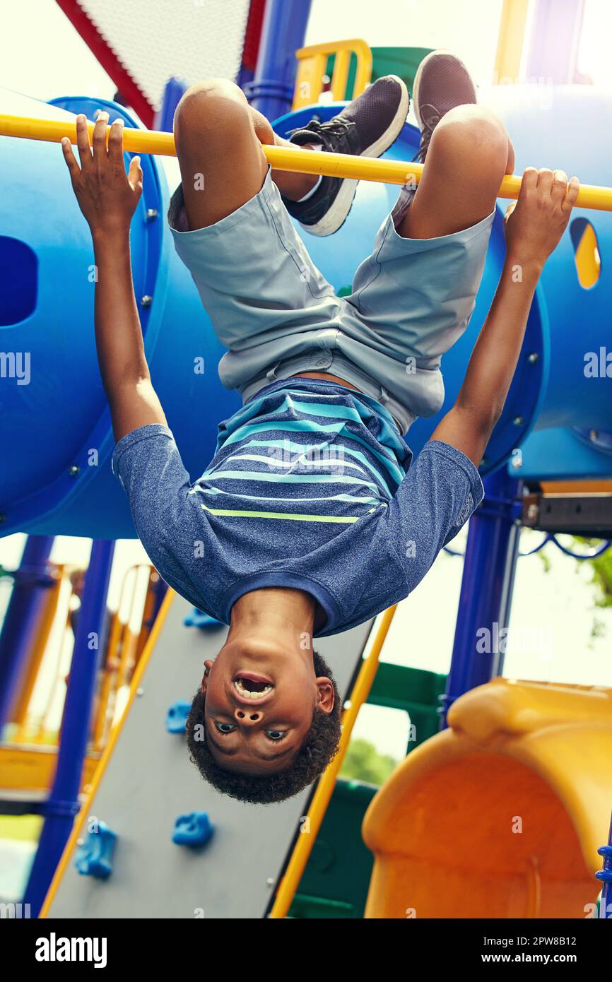 Les enfants voient la vie différemment. un jeune garçon suspendu à l'envers sur une salle de gym dans la jungle dans le parc. Banque D'Images