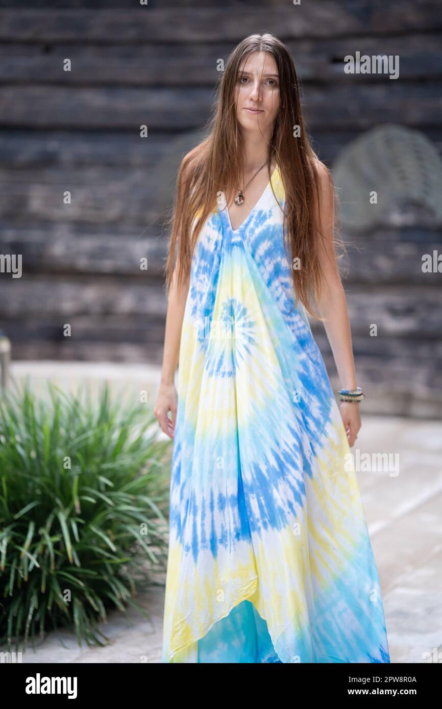 Une magnifique femme aux cheveux ondulés brillants dans une élégante robe d'été décontractée pose pour l'appareil photo Banque D'Images