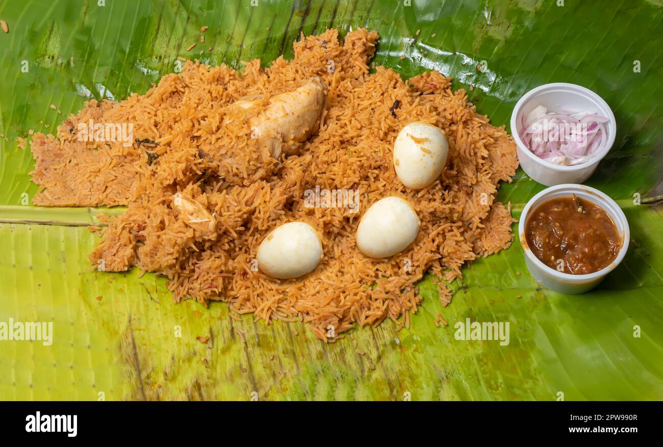 Poulet biryani servi avec de la raita et des oignons sur une feuille de banane. Un plat indien non végétarien populaire Banque D'Images