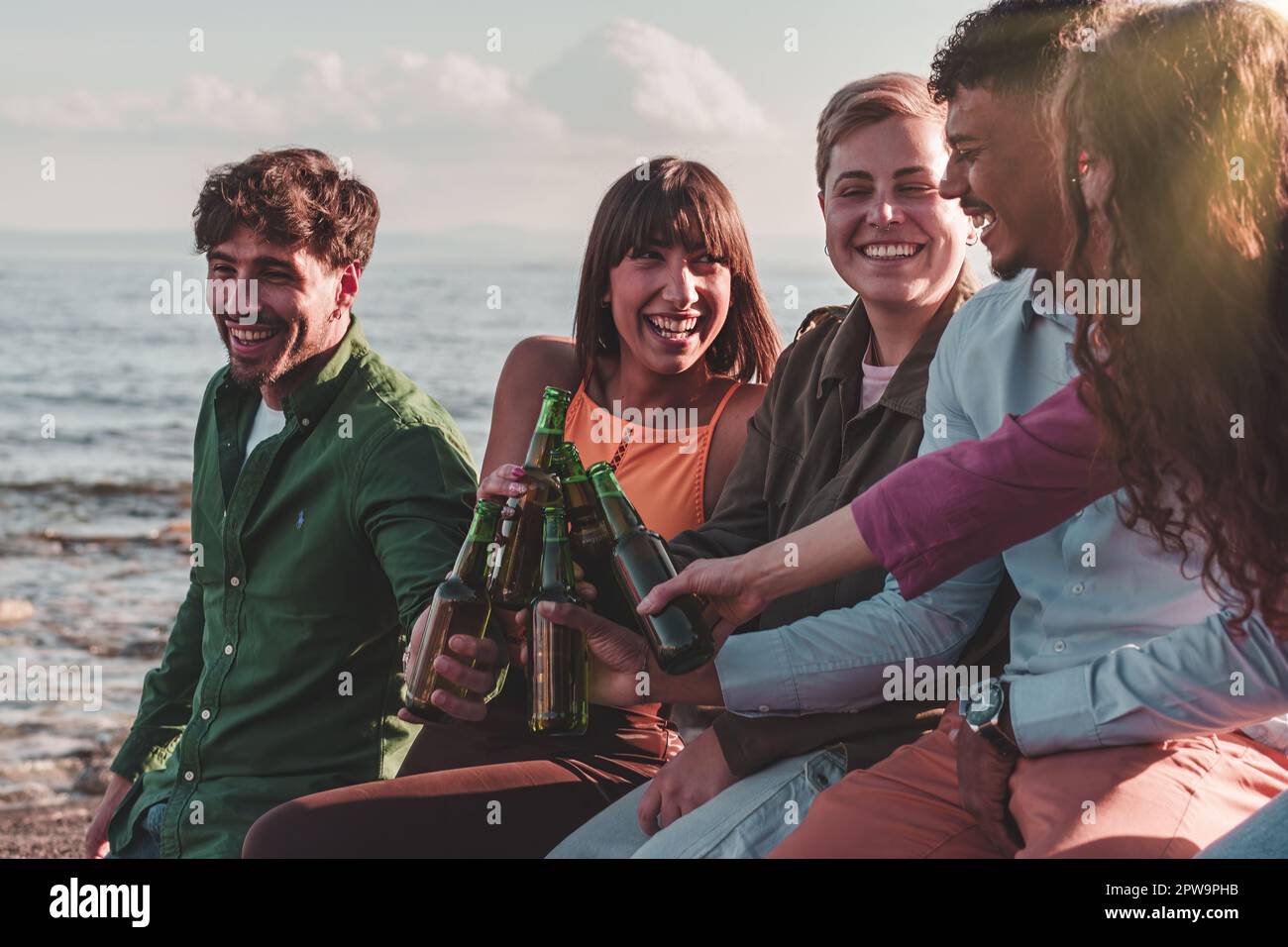 Divers groupes d'amis en buvant des bouteilles de bière tout en étant assis sur une rive rocheuse au bord de la mer. Banque D'Images