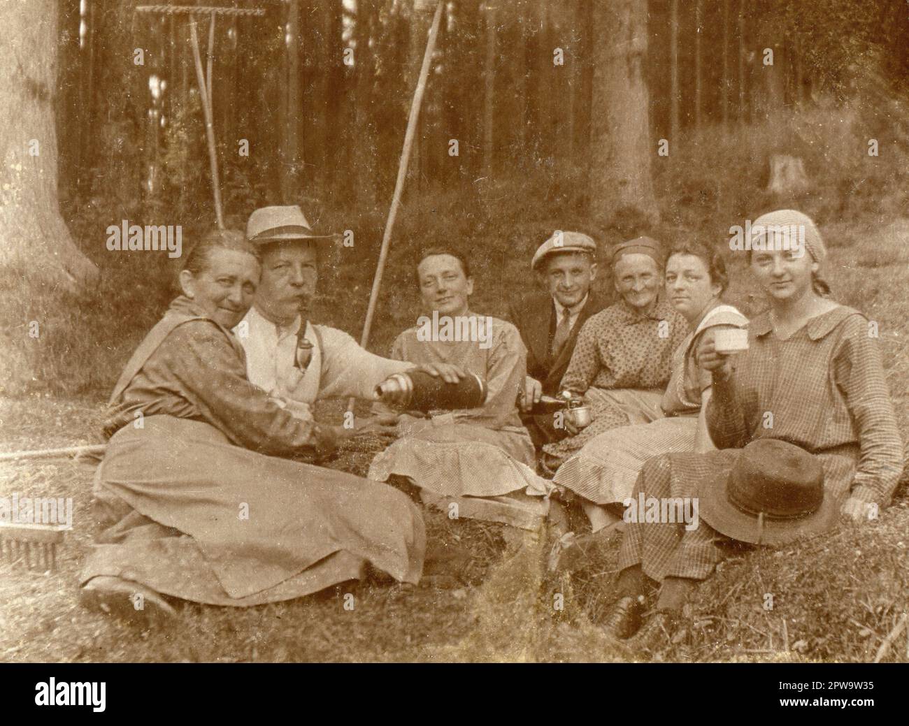 Silésie supérieure. 1930s. Un groupe de travailleurs agricoles prenant une pause au bord d'une zone boisée. Le monsieur plus âgé fume un tuyau traditionnel de chasseur en porcelaine et verse des boissons dans une fiole à vide. Les râteaux de foin en bois sont visibles en arrière-plan. Banque D'Images