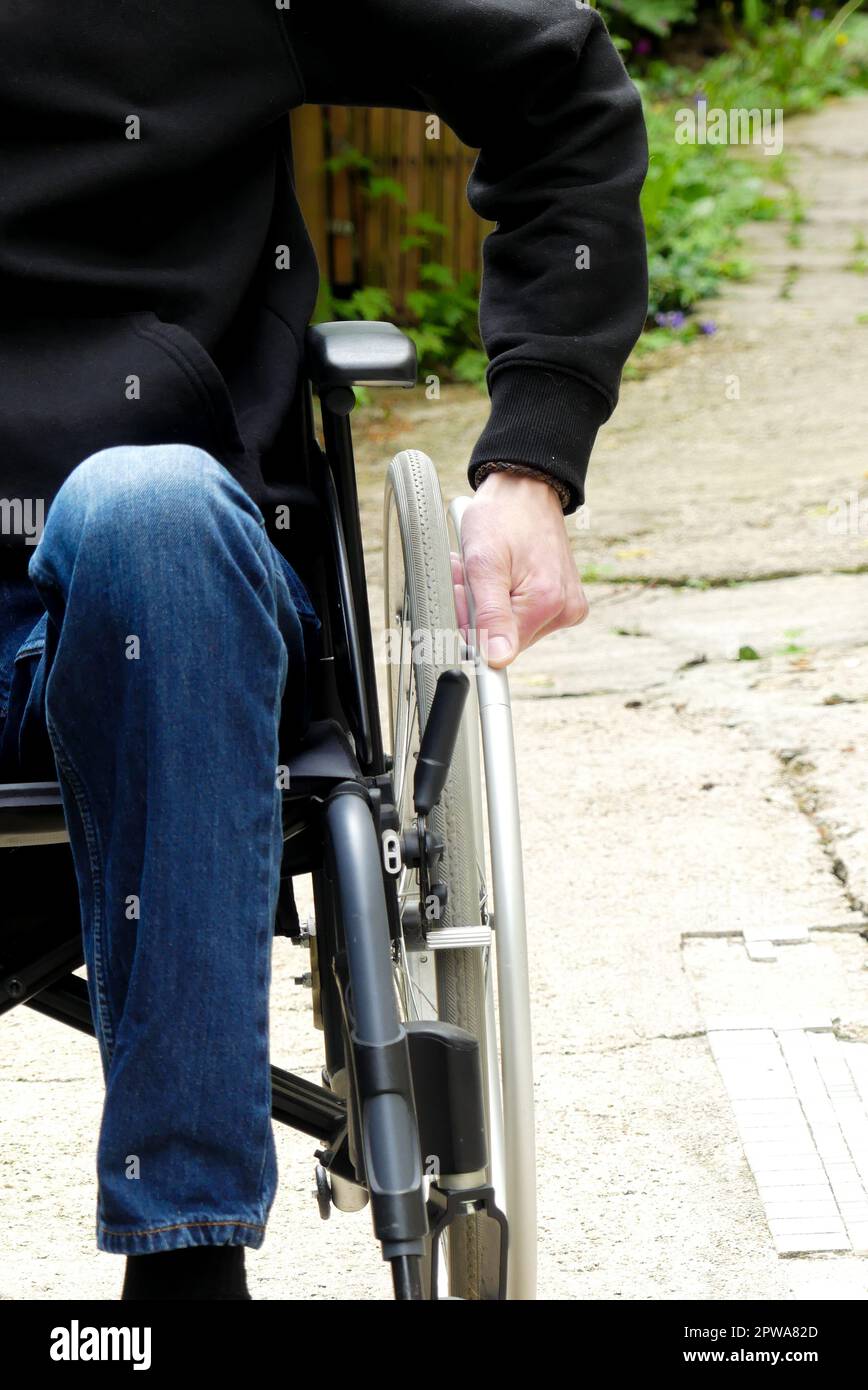 Personne handicapée en fauteuil roulant. Un homme à mobilité réduite dans une allée avec végétation. Banque D'Images