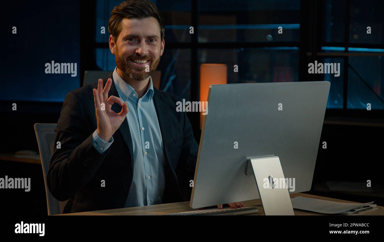 Joyeux homme d'affaires caucasien adulte d'âge moyen homme patron chef travail sur ordinateur dans le soir bureau développer en ligne projet regardant la caméra Banque D'Images