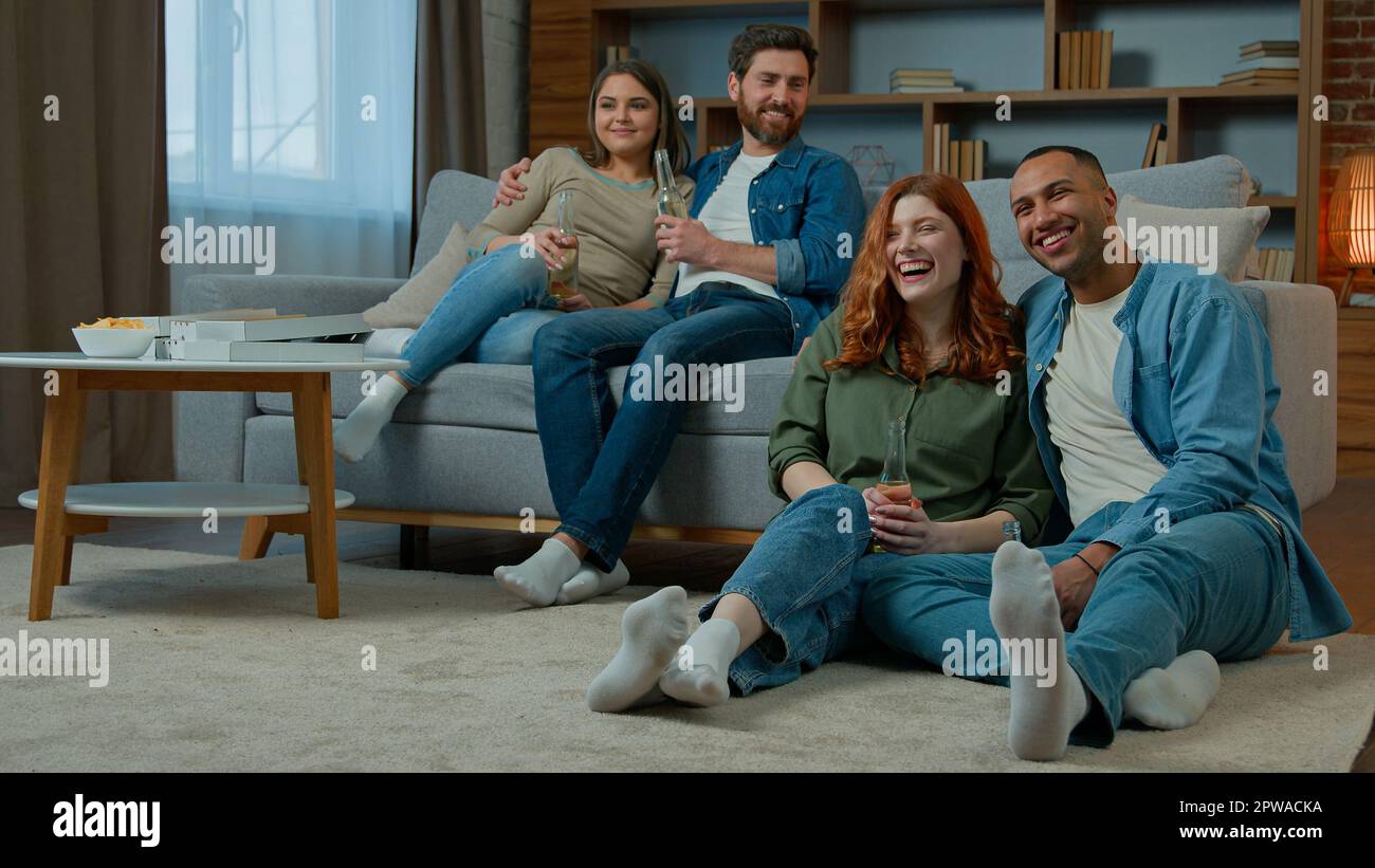 Amis multiraciaux hommes femmes regardant la télévision à la maison couple hispanique se détendre sur un canapé famille afro-américaine caucasienne s'asseoir sur le sol profiter de la télévision Banque D'Images