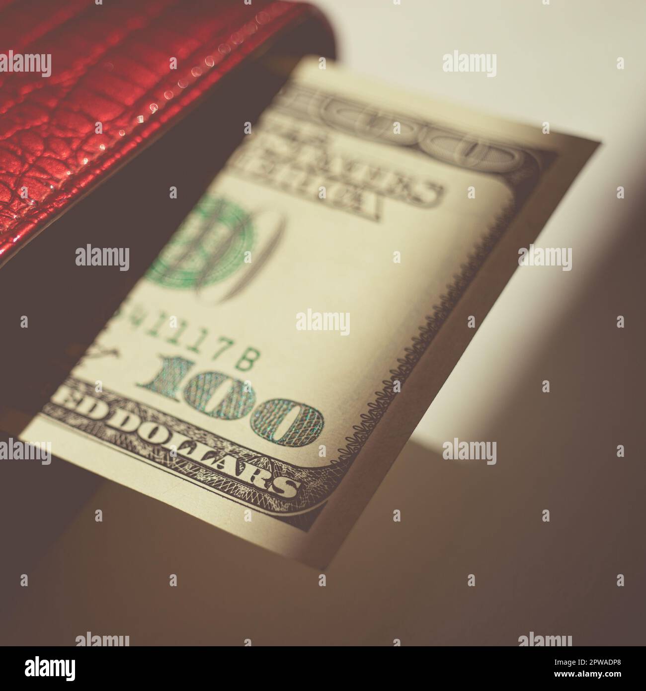 Une facture de cent dollars qui colle d'un sac à main rouge sur une table  grise ensoleillée avec de fortes ombres Photo Stock - Alamy
