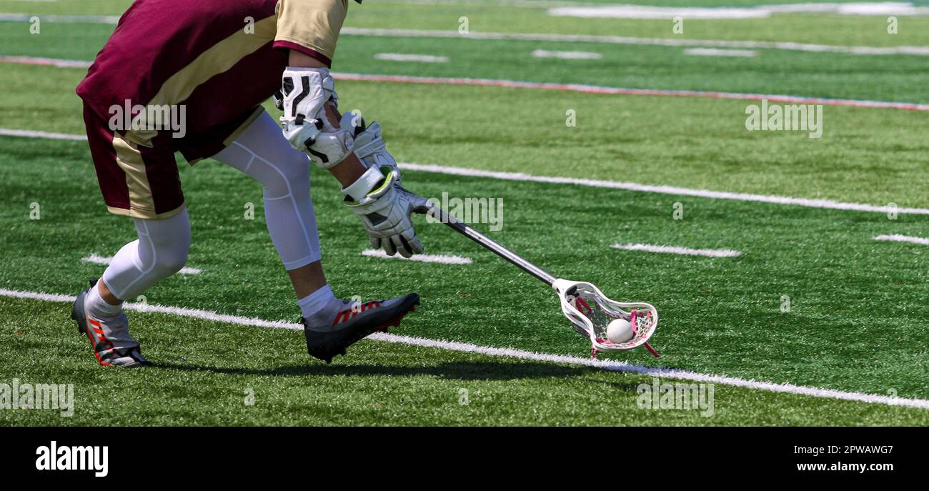 Un joueur de crosse d'école secondaire est en train de courir et de ramasser le ballon pendant un match. Banque D'Images