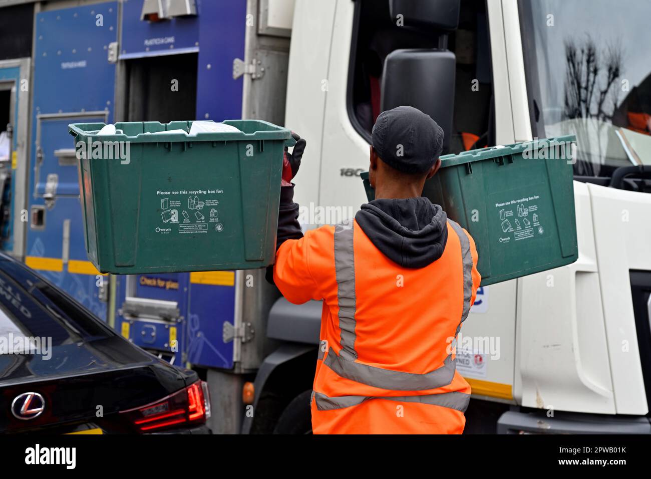 Un ouvrier du conseil transportant deux boîtes en plastique de matériaux de recyclage vers un camion de recyclage Banque D'Images