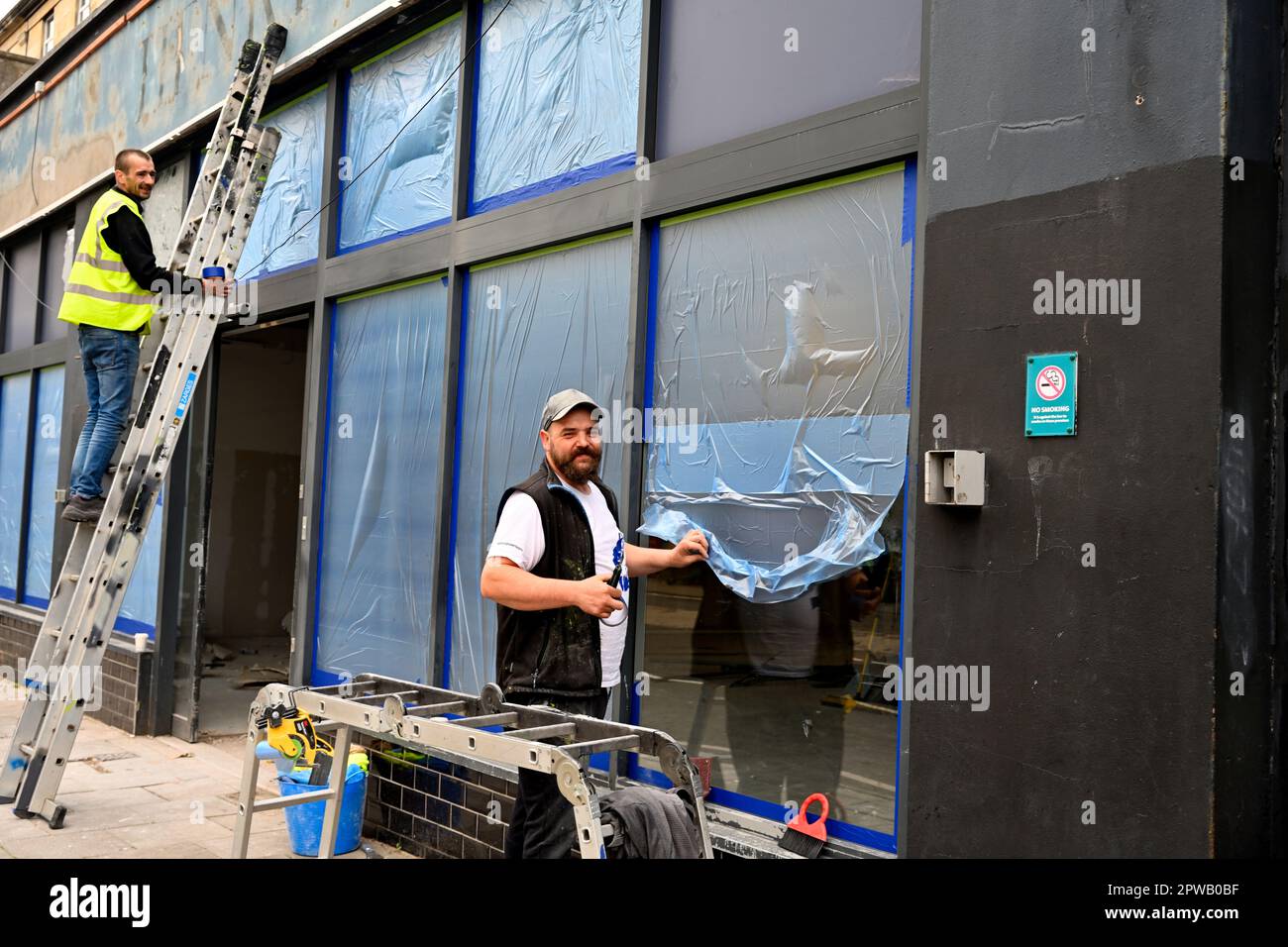Workman pose une feuille de masquage de protection en plastique sur la fenêtre en verre de l'atelier en vue de la peinture par pulvérisation Banque D'Images