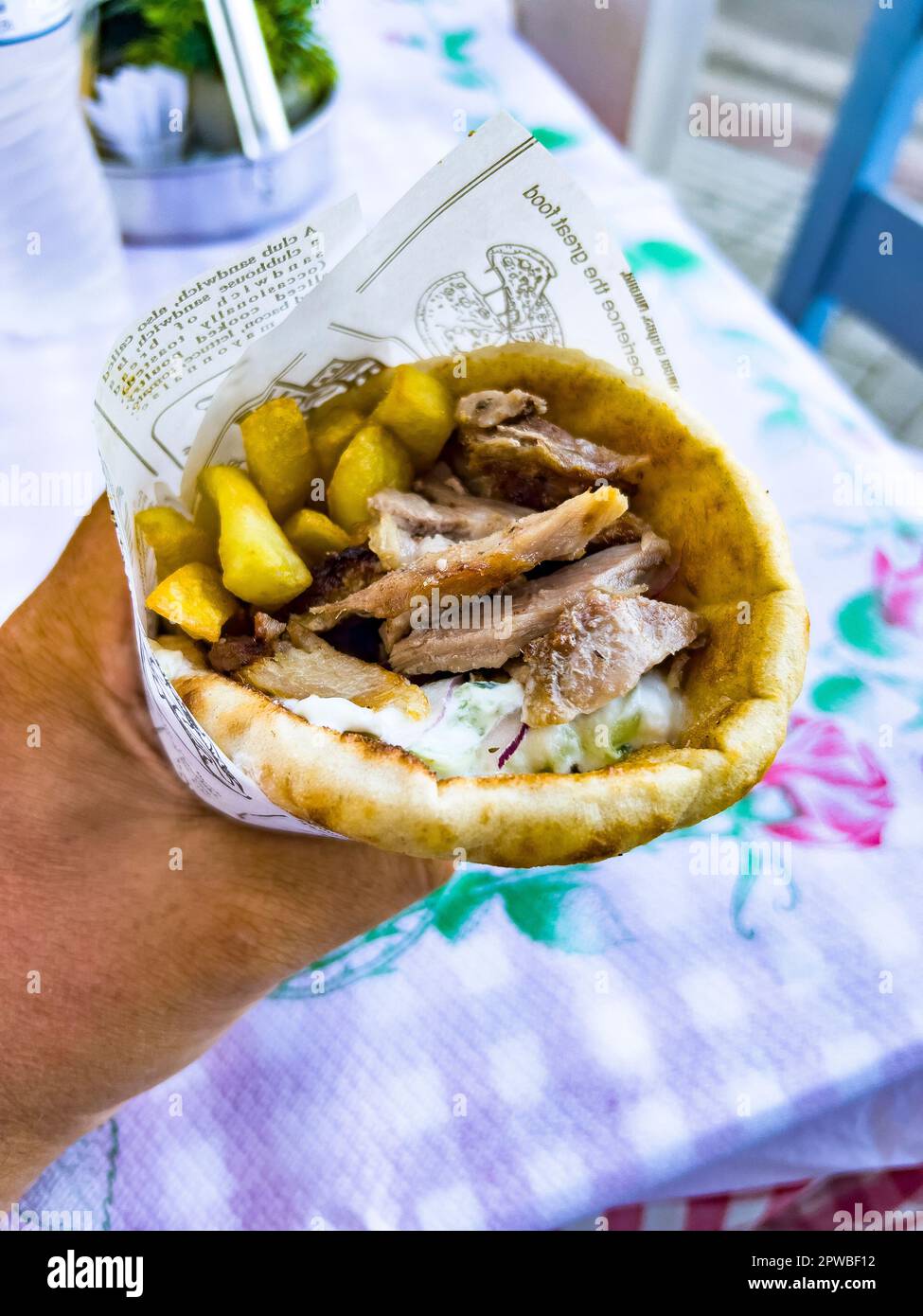 Main humaine tenant un gyros à la viande grecque enveloppé de pain pita et servi avec des pommes de terre frites et de la sauce tzatziki. Destination de voyage et alimentation Banque D'Images