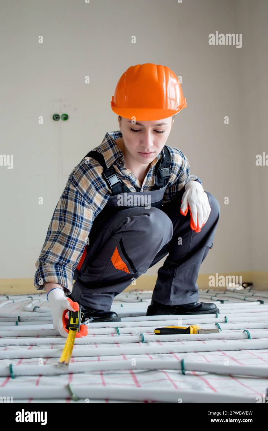 Une travailleuse de construction vérifie l'installation d'un plancher chaud  avec un mètre ruban sur le chantier Photo Stock - Alamy