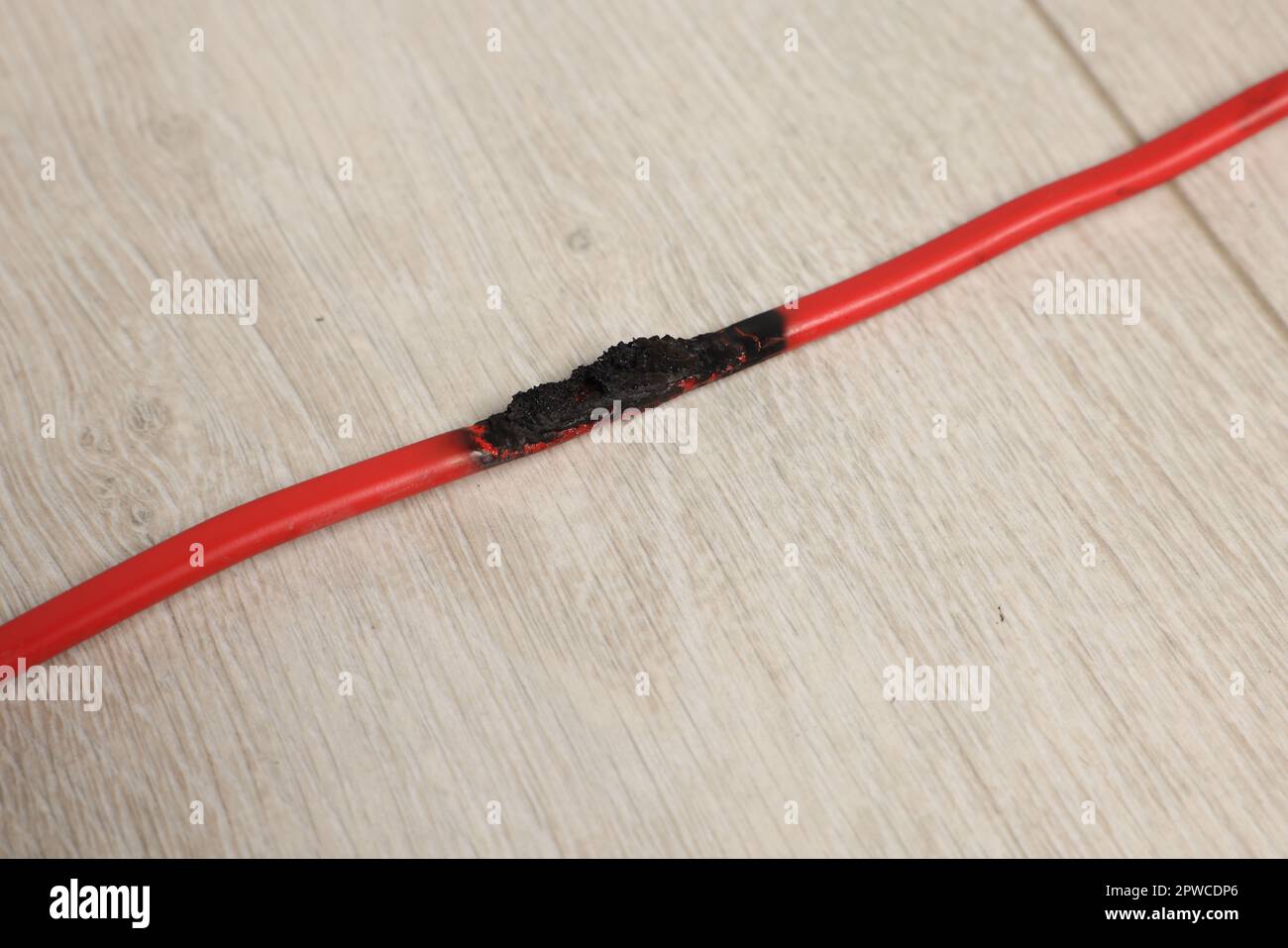 Fil rouge brûlé sur parquet, gros plan. Court-circuit électrique Banque D'Images