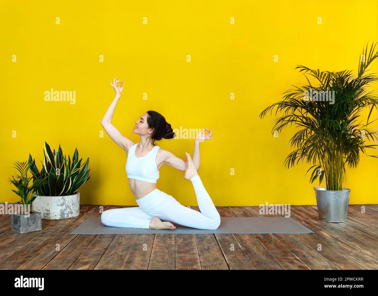 Jeune femme brunette en vêtements de sport blancs sur tapis et faisant du yoga tout en pratiquant la pleine conscience Banque D'Images