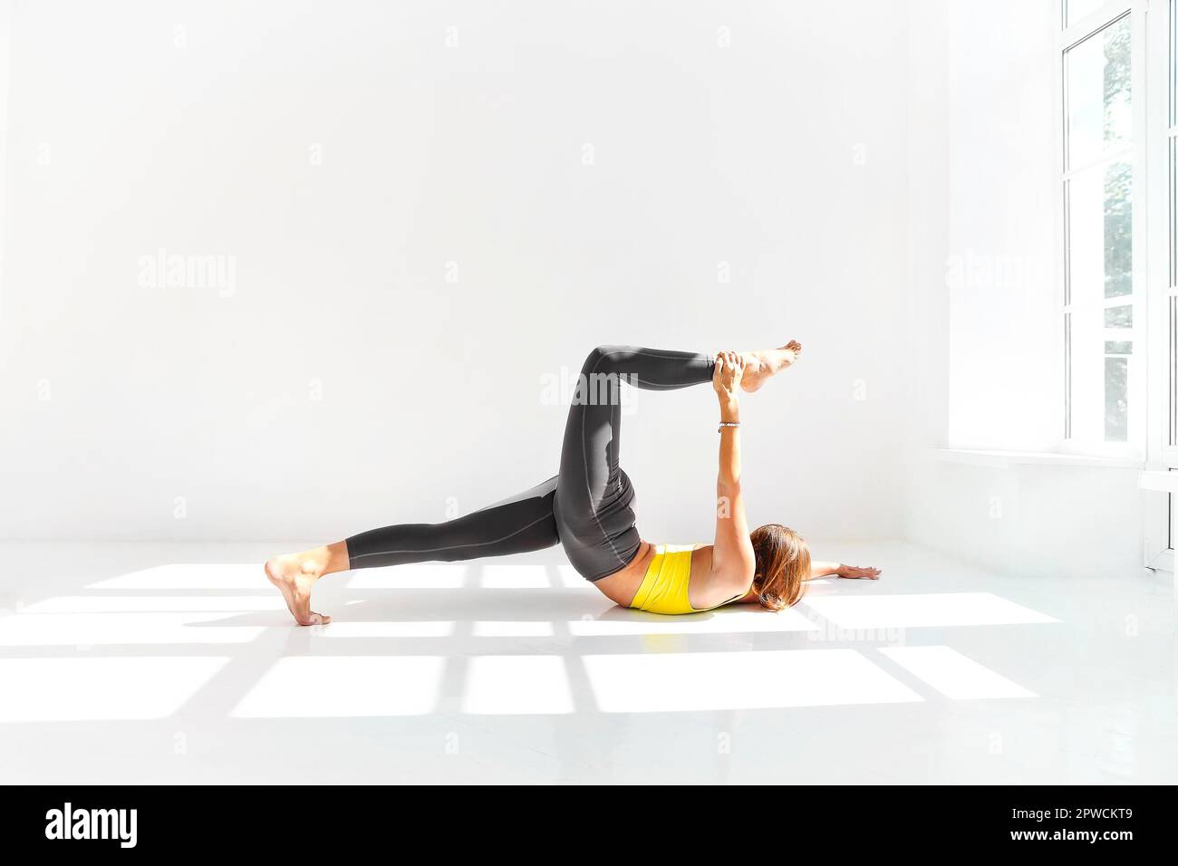 Vue latérale de la femme calme dans les vêtements de sport pratiquant le yoga pendant equilibrage sur les bras sur le tapis et vue à l'écart Banque D'Images