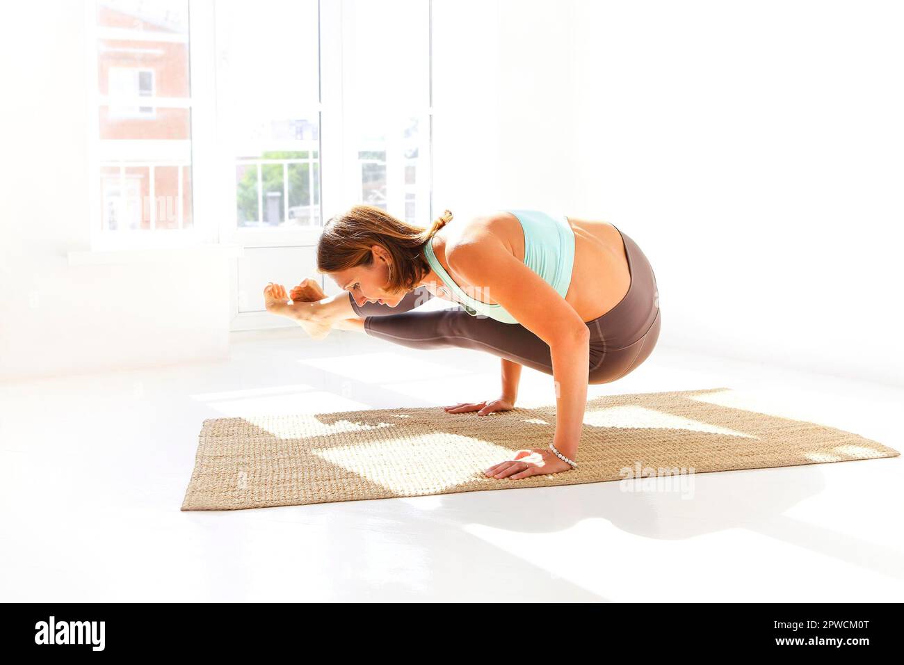 Vue latérale de la femme calme dans les vêtements de sport pratiquant le yoga Pompier pose tout en équilibrant les bras sur le tapis et en regardant loin Banque D'Images