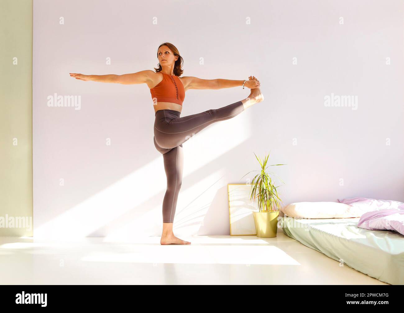 Vue latérale de la femme calme dans les vêtements de sport pratiquant le yoga dans la posture de Firefly tout en équilibrant et en regardant loin Banque D'Images
