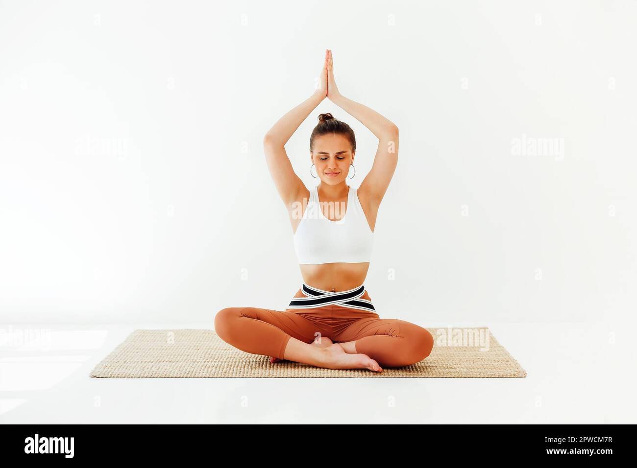 Jeune femme brunette dans les vêtements de sport assis sur le tapis et faisant le yoga tout en pratiquant la pleine conscience. Concept de santé physique et mentale Banque D'Images