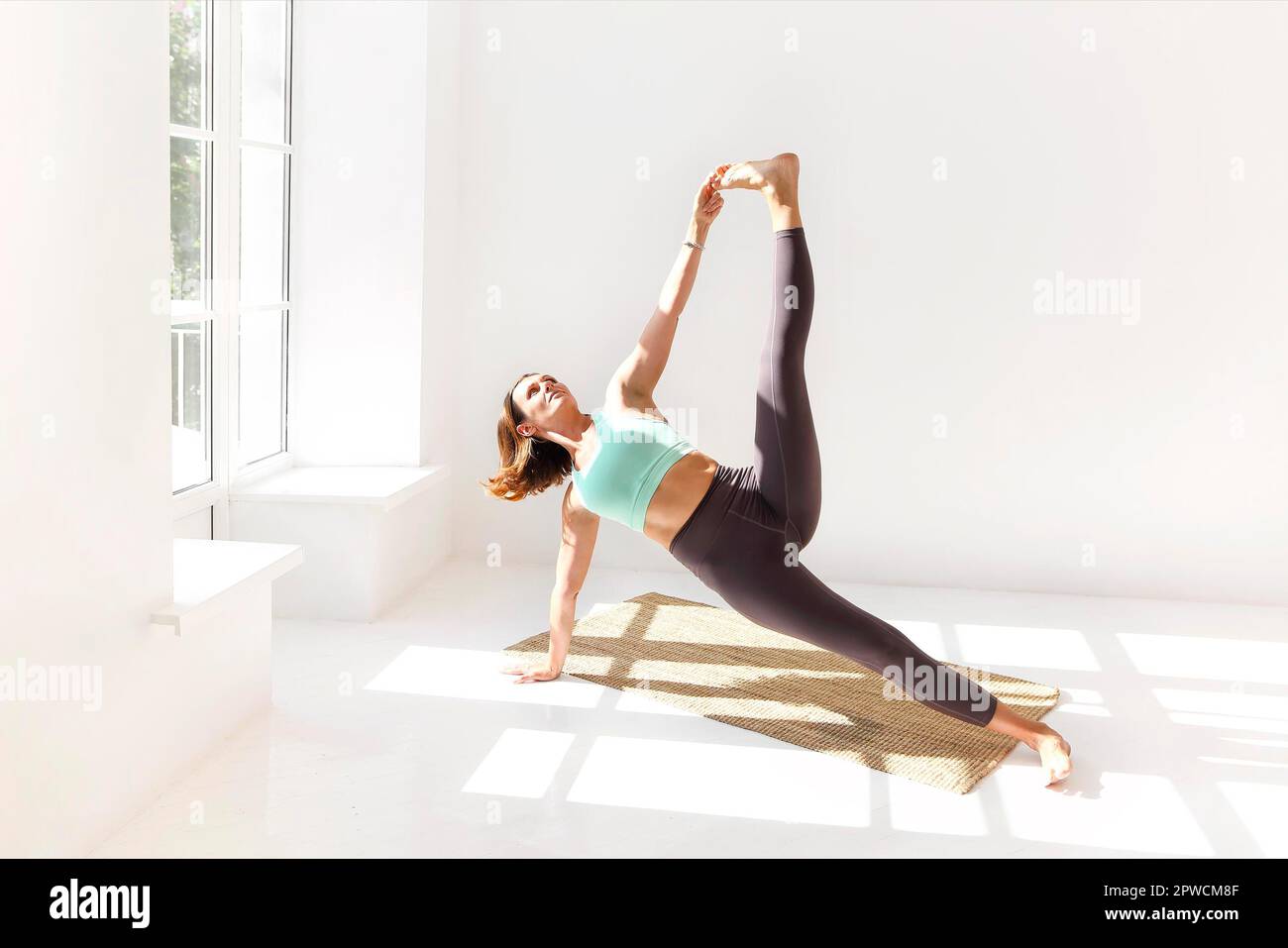 Vue latérale de la femme calme dans les vêtements de sport pratiquant le yoga Pompier pose tout en équilibrant les bras sur le tapis et en regardant loin Banque D'Images