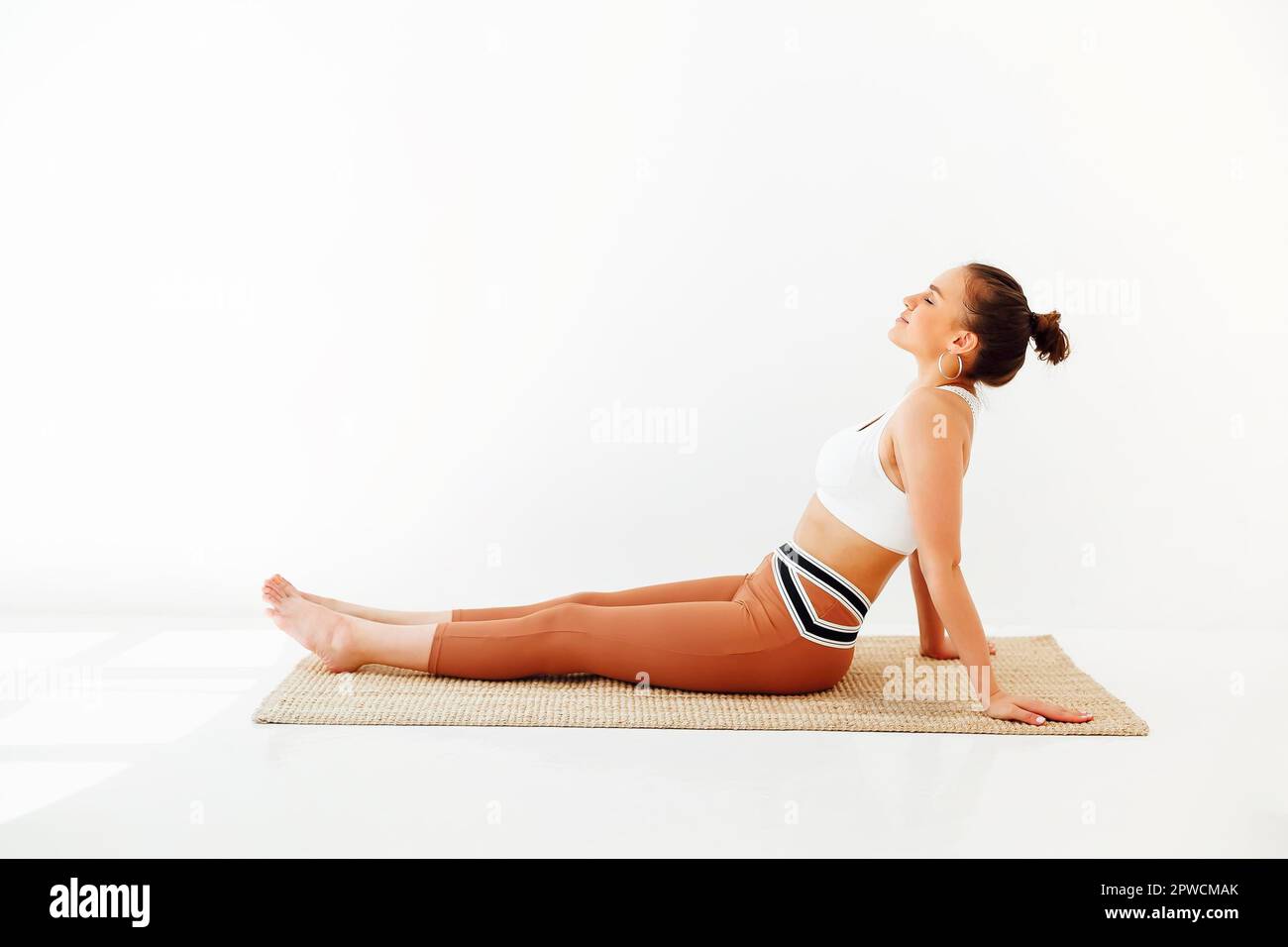 Jeune femme brunette dans les vêtements de sport assis sur le tapis et faisant le yoga tout en pratiquant la pleine conscience. Concept de santé physique et mentale Banque D'Images