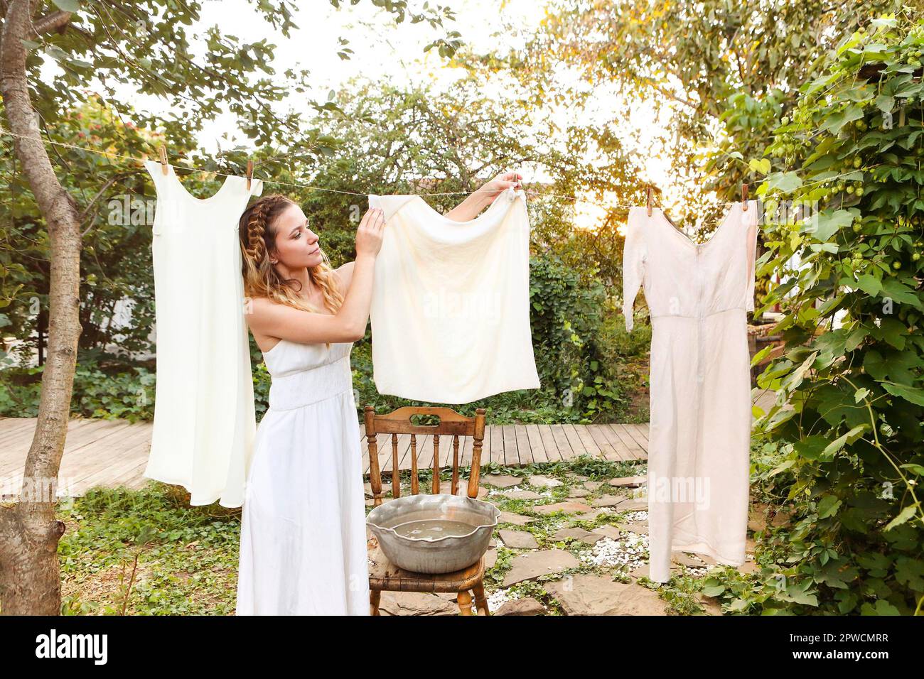 Jeune femme qui pendait du linge à l'extérieur. Mignonne fille en robe laver les vêtements blancs dans le lavabo en métal dans l'arrière-cour, pendant la lessive sur la corde à linge et de quitter Banque D'Images