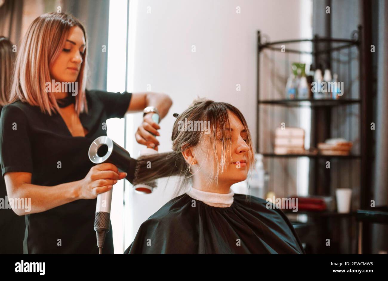 Une femme heureuse avec la styliste qui fait une coiffure au salon. Coiffeur féminin compétent décider quoi faire dans un salon de coiffure avec une cliente brune. Deux Banque D'Images