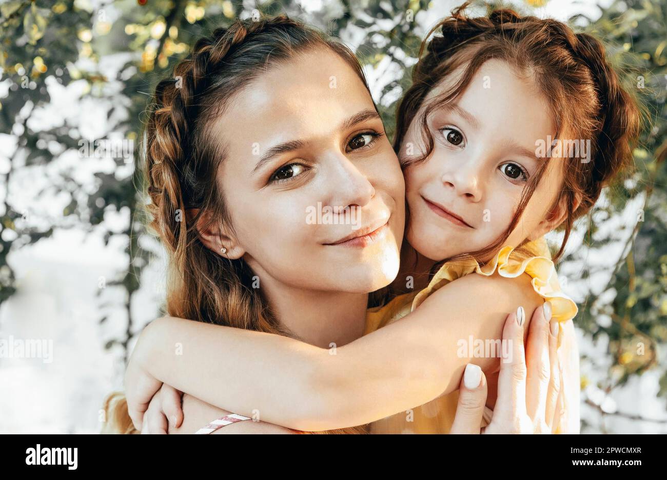 Maternité et maternité aimante. Belle jeune maman avec des cheveux tressés embrassant sa jolie petite fille douce tout en passant du temps ensemble à l'extérieur Banque D'Images