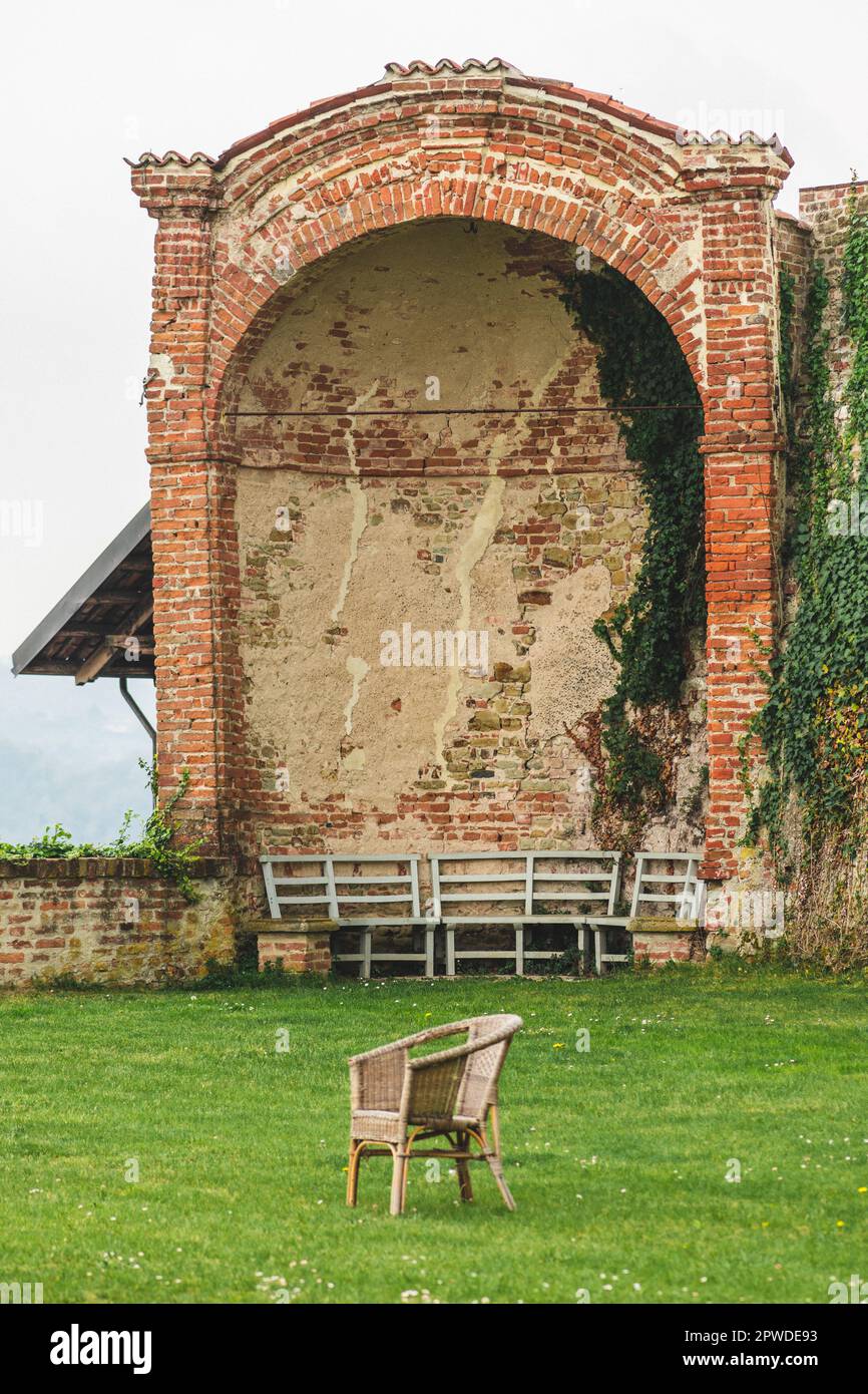 Ancien fauteuil en osier vide sur pelouse en herbe verte et vieux mur en brique avec ruines d'une chapelle sur fond, vertical Banque D'Images