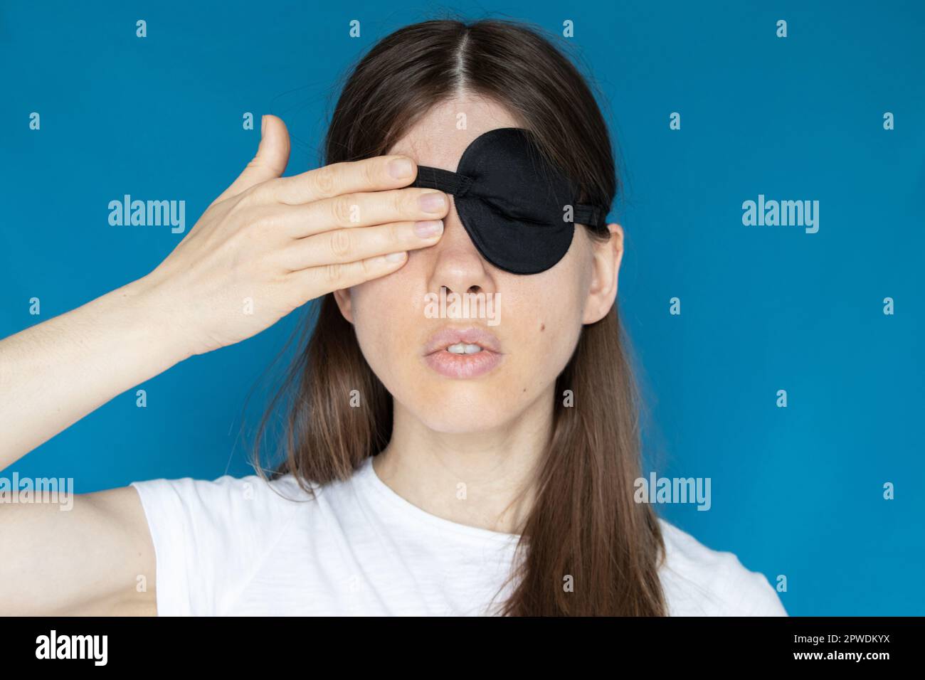 Une fille avec un bandage sur un oeil et l'autre oeil fermé avec sa main sur un fond bleu, ne voyez pas, ne regardez pas Banque D'Images