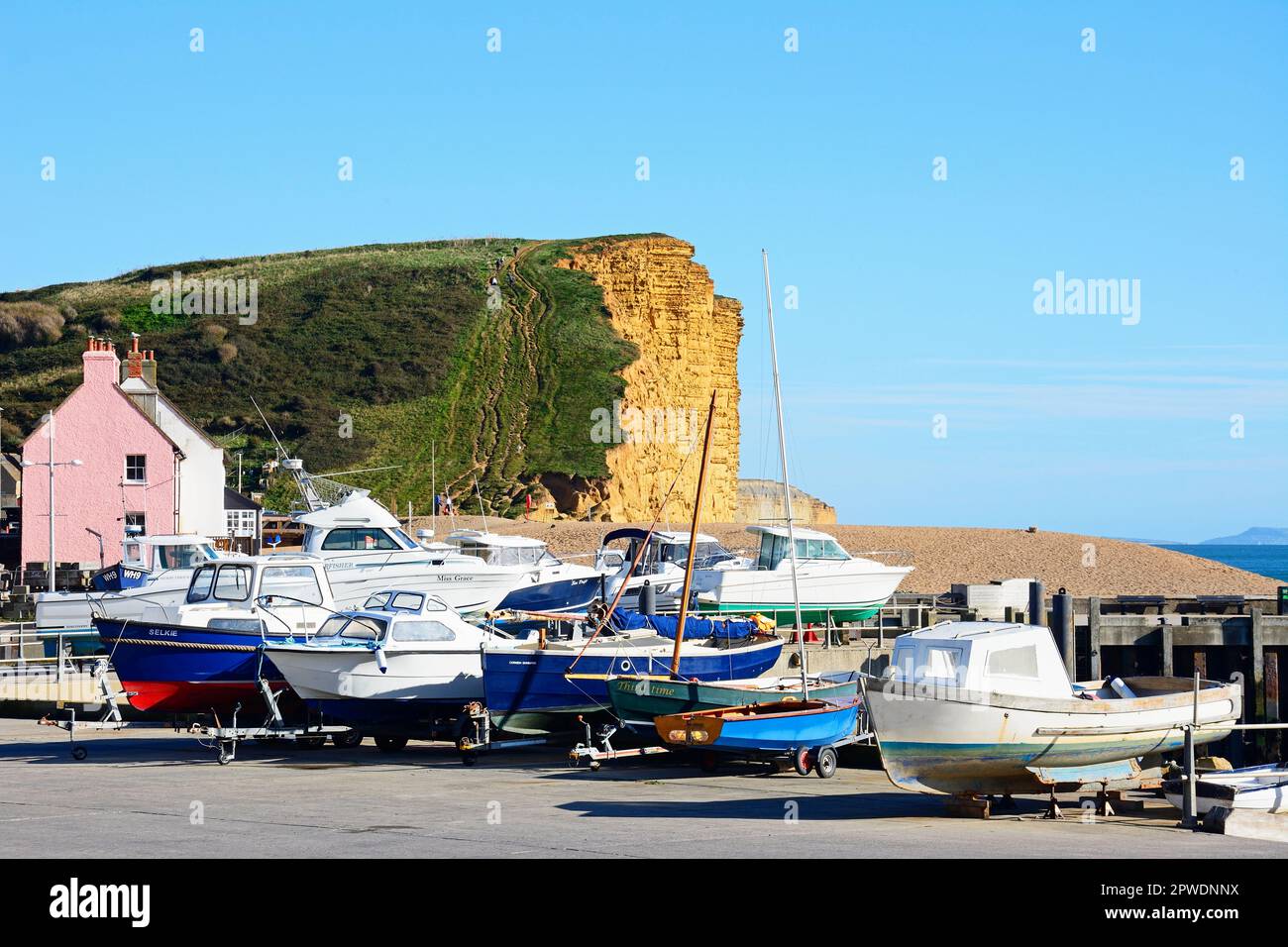 Bateaux dans le quai sec le long de la promenade de la jetée avec vue sur la plage de galets et les falaises de Jurassic Coast, West Bay, Dorset, Royaume-Uni. Banque D'Images