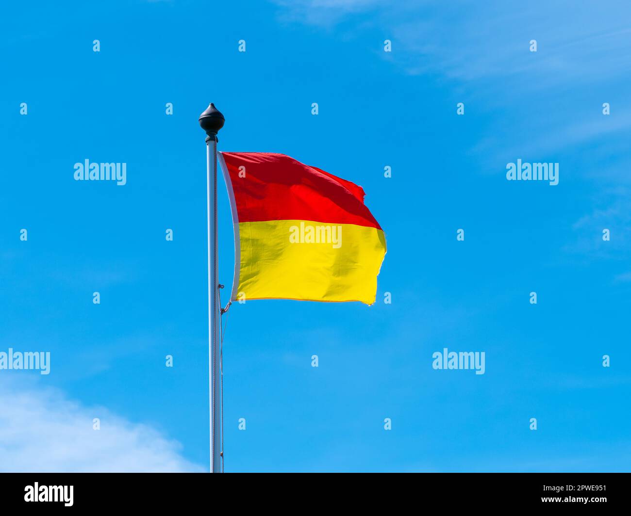 Un drapeau rouge et jaune permettant de nager sur la plage. Un drapeau sur fond bleu ciel. Banque D'Images Un drapeau rouge et jaune permettant de nager sur la plage. Un drapeau sur fond bleu ciel. Banque D'Images