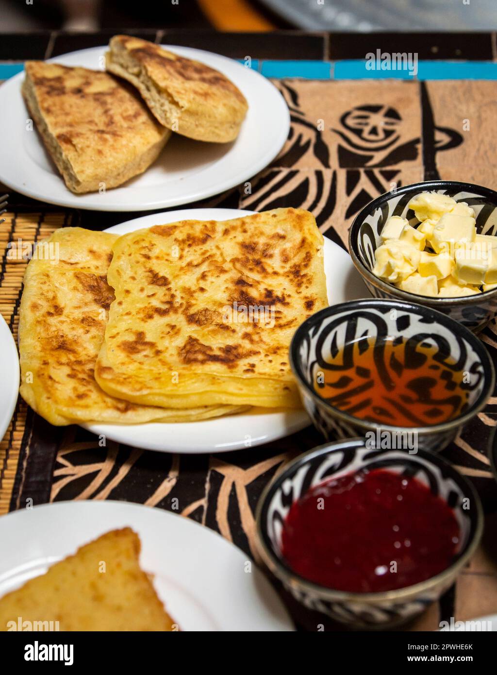 Petit-déjeuner marocain traditionnel avec crêpes, pain, beurre, miel et confiture placés sur la table à manger Banque D'Images