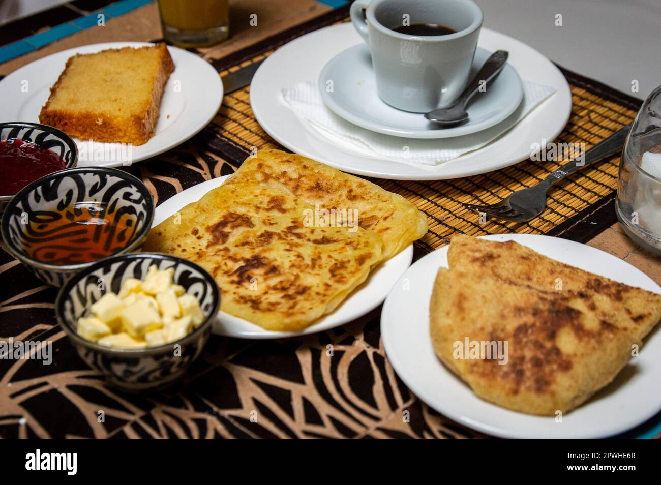 Petit-déjeuner marocain traditionnel avec crêpes, café, pain, beurre, miel et confiture placés sur la table à manger Banque D'Images