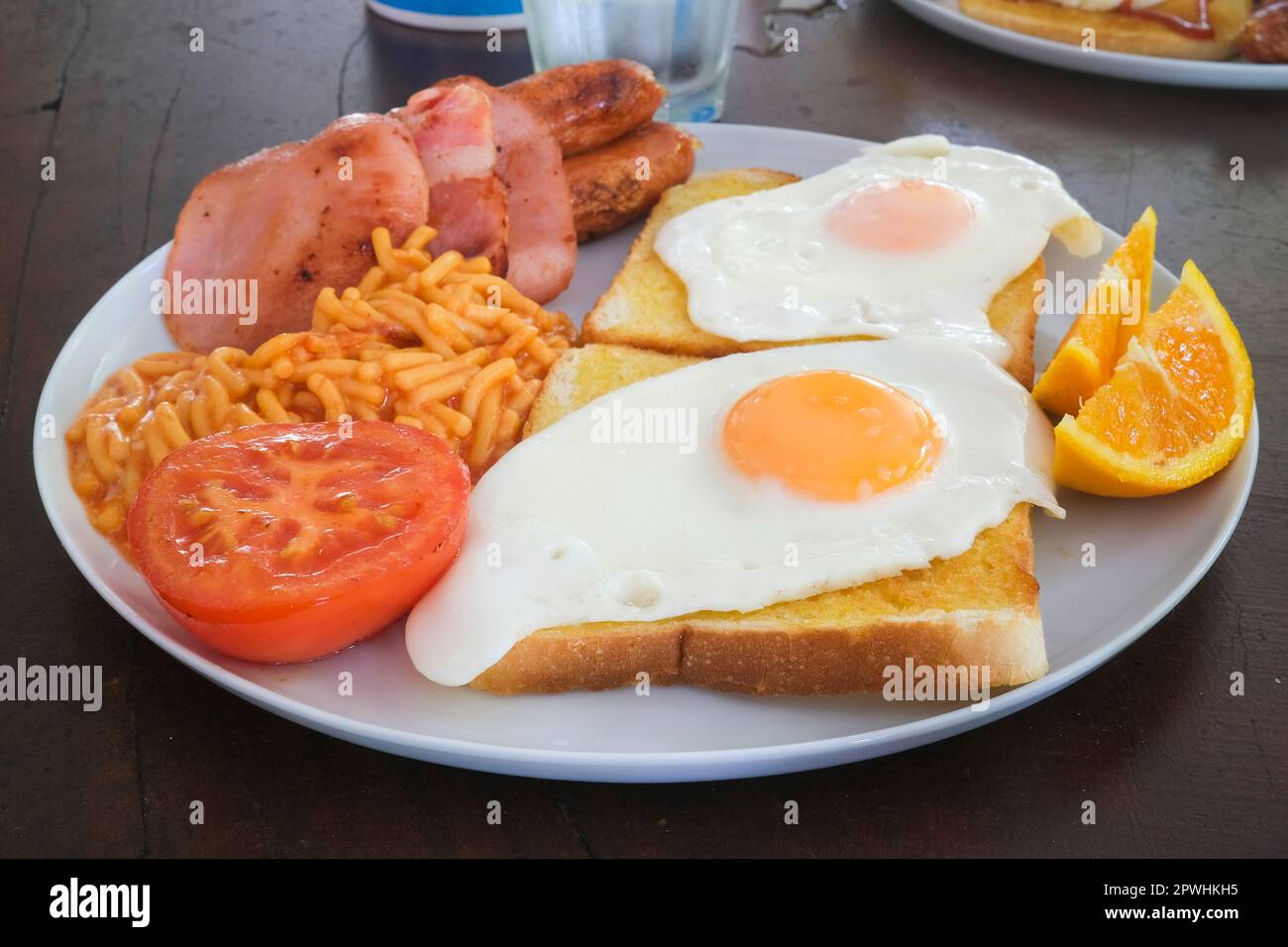 Petit-déjeuner australien avec œufs sur pain grillé, bacon, saucisses, spaghetti, tomates et tranches d'orange Banque D'Images