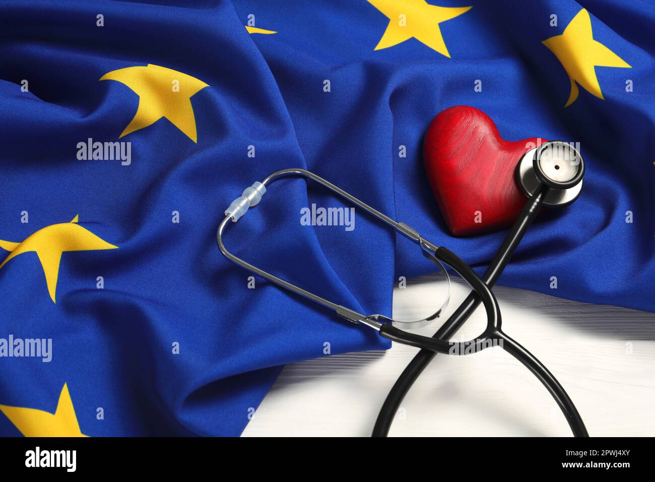 Stéthoscope, coeur rouge et drapeau de l'Union européenne sur table blanche en bois Banque D'Images