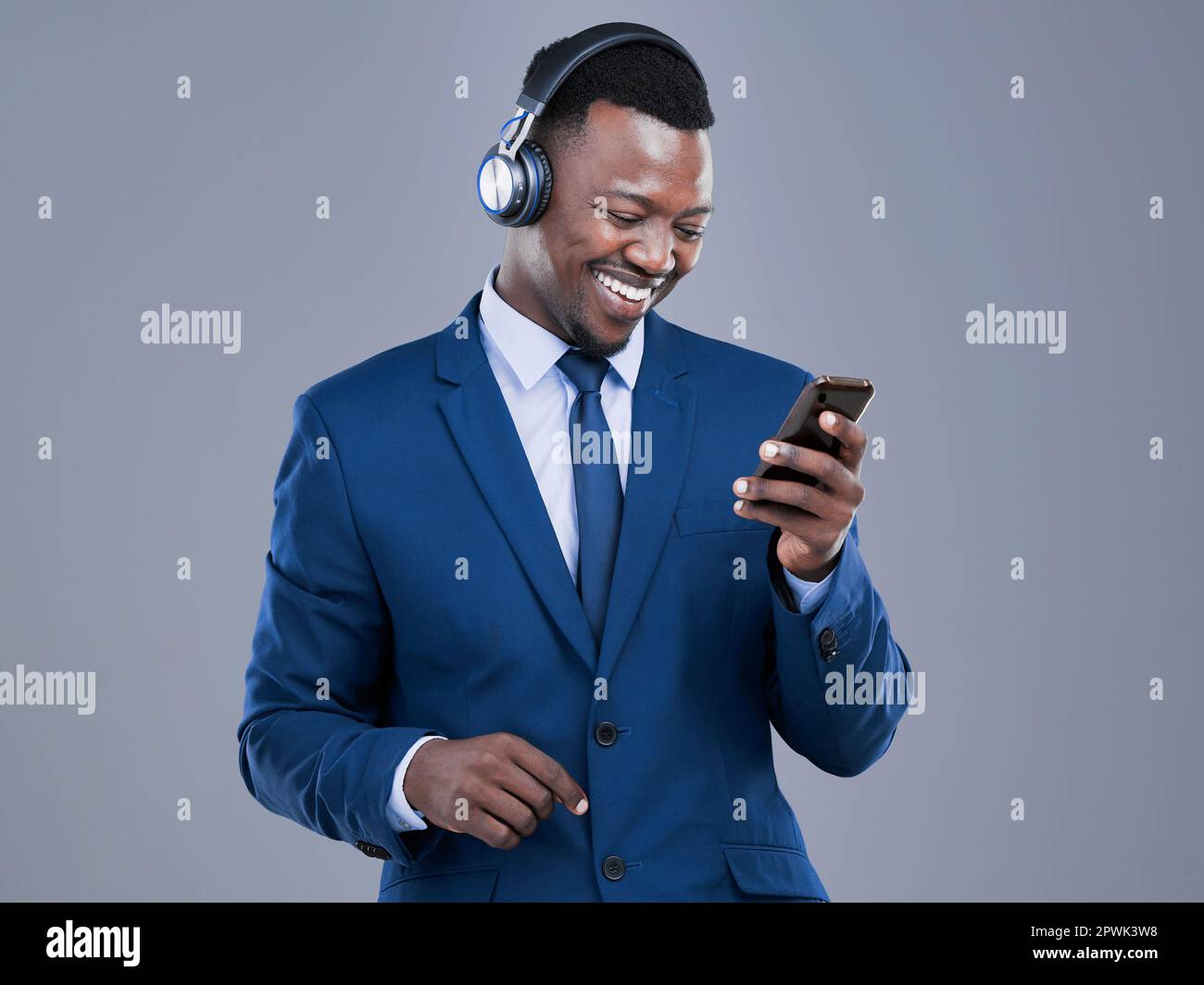 Accéder à ses listes de lecture préférées. un beau jeune homme d'affaires utilisant son téléphone portable pour écouter de la musique en studio sur fond gris Banque D'Images