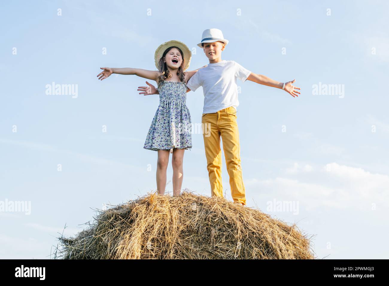 Portrait des enfants garçon et fille restant et s'embrassant, chantant des chansons, agitant les mains jouant le singe sur haystack dans le champ.Journée ensoleillée.Vêtements pour enfants Banque D'Images