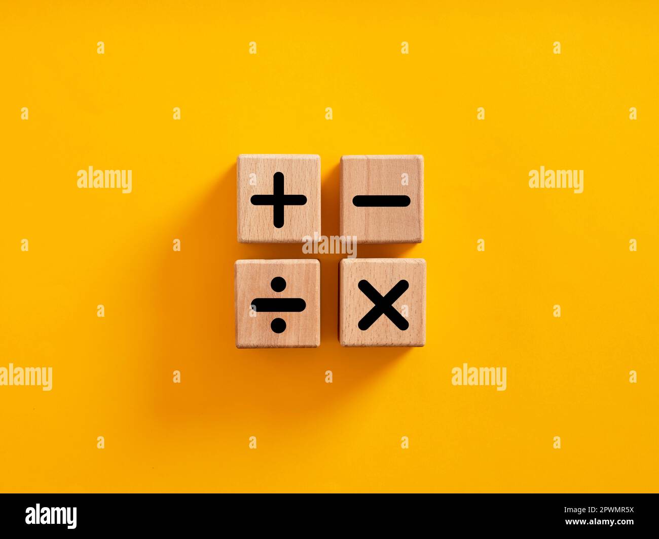 Symboles des opérations mathématiques de base. Plus, moins, multipliez et divisez les symboles sur des cubes en bois sur fond jaune. Formation mathématique ou mathématique et Banque D'Images