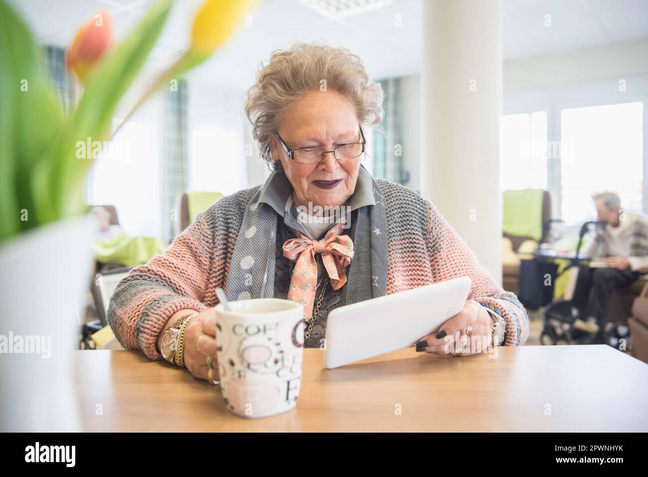 Femme âgée utilisant une tablette numérique tout en buvant du café Banque D'Images
