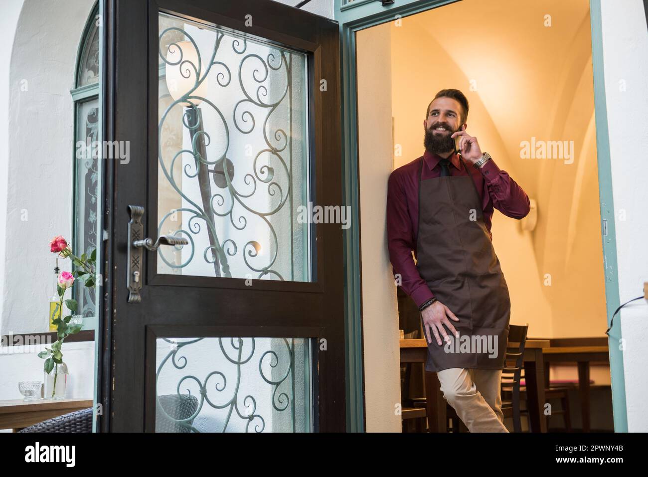 Jeune entrepreneur parlant au téléphone en se tenant à la porte du restaurant Banque D'Images