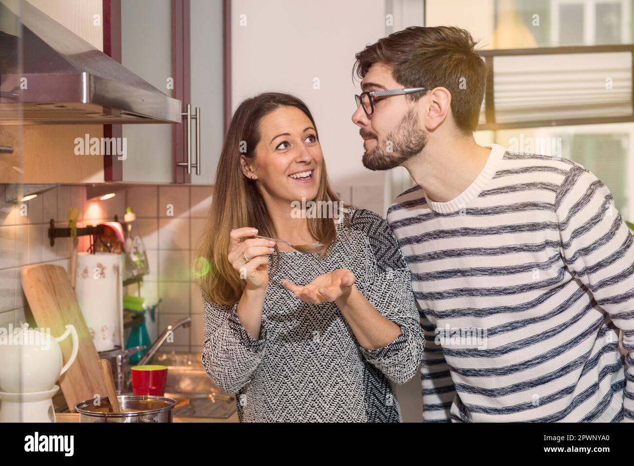 La femme goûte la soupe dans la cuisine pendant que son mari regarde, Munich, Allemagne Banque D'Images