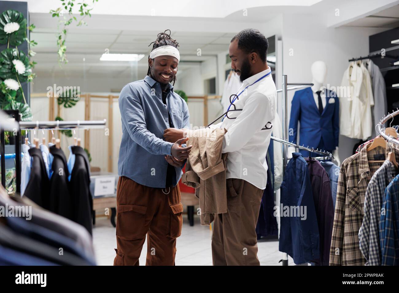 Homme souriant essayant de porter un maillot et discutant des tendances de  la mode avec un vendeur en magasin. Un client du centre commercial  afro-américain porte des vêtements modernes dans une boutique