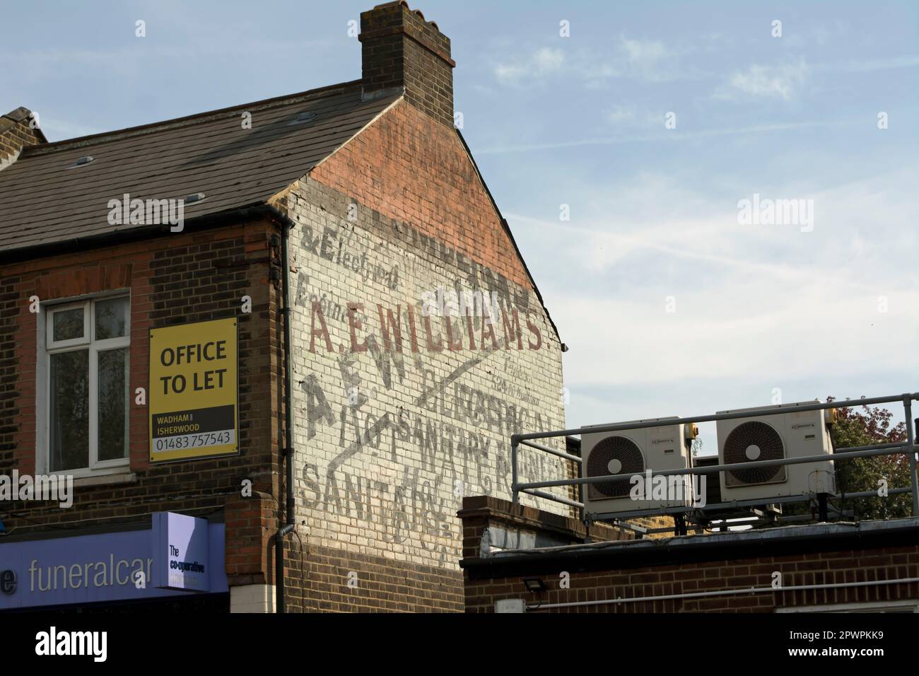 panneau fantôme sur un bâtiment dans le parc de raynes, sud-ouest de londres, angleterre, publicité par ex. williams, électricité, ingénieur en eau chaude et assainissement Banque D'Images