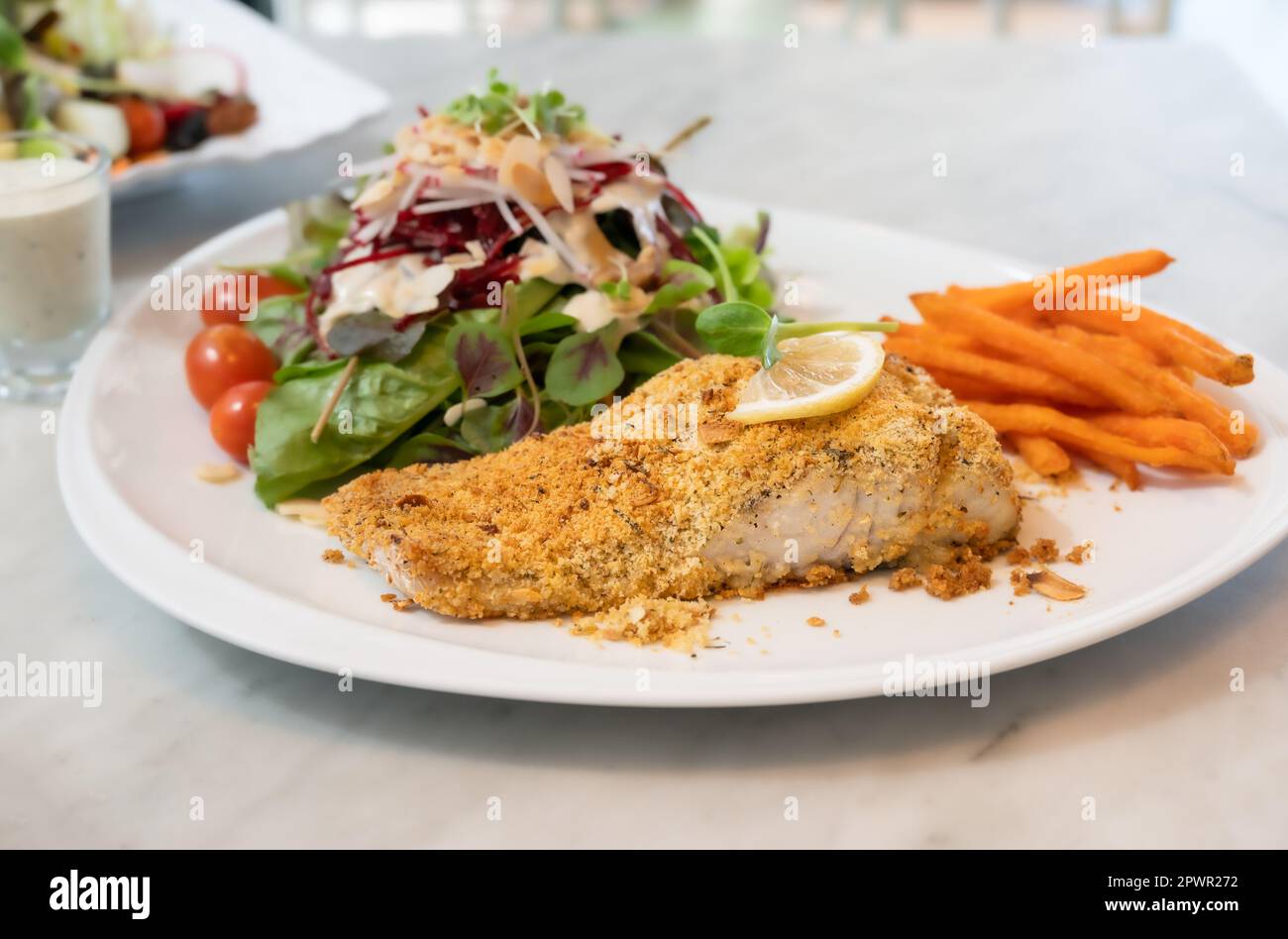 Steak de poisson grillé au bar avec croûte d'herbes et légumes sur une assiette blanche Banque D'Images