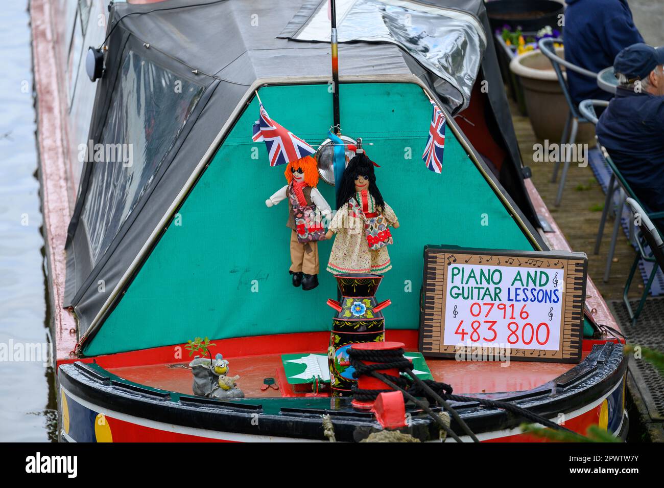Panneau à côté de deux poupées sur l'arc d'un bateau de narrowboat amarré offrant des leçons de guitare et de piano. Banque D'Images