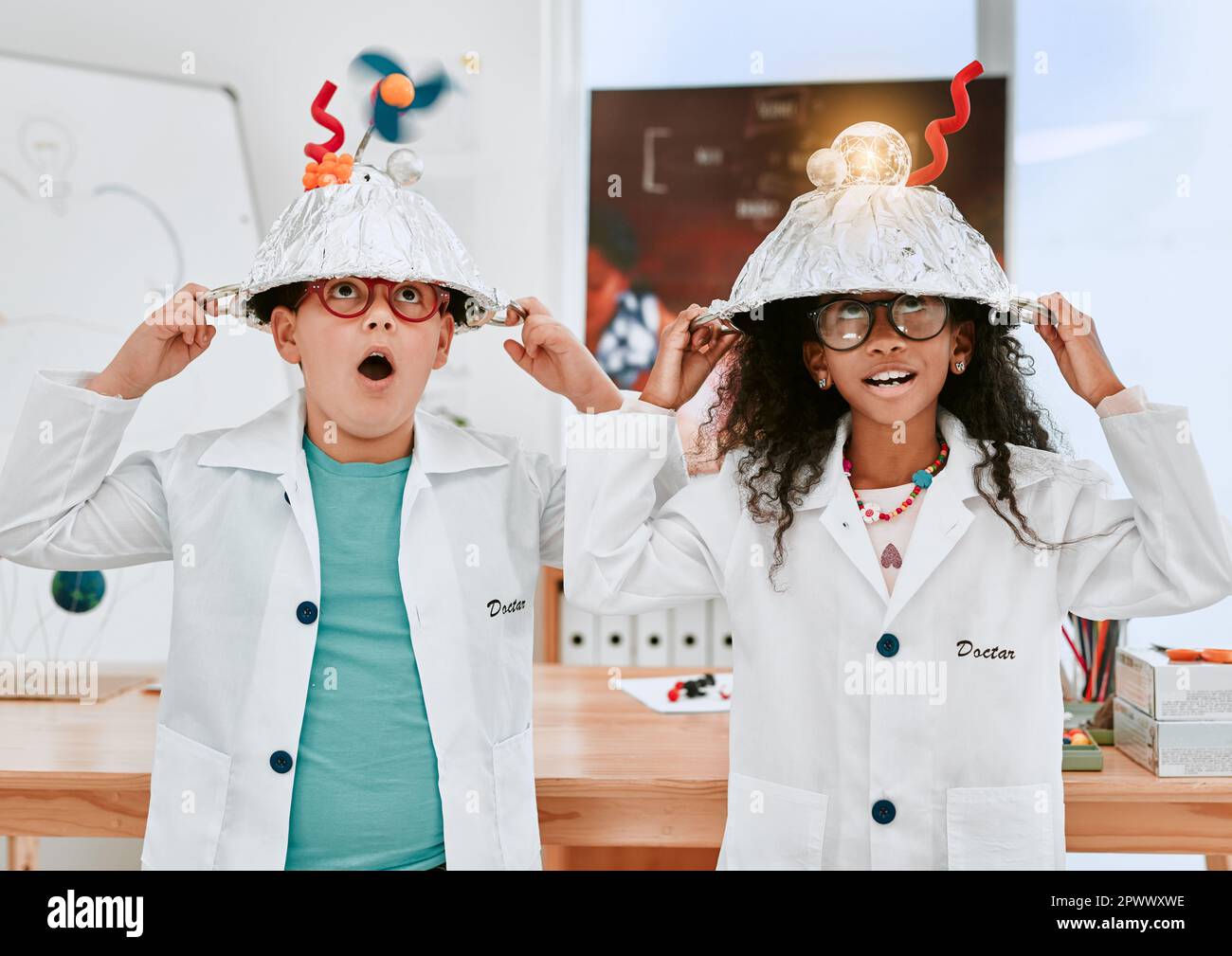 Le professeur a déclaré que nous devrions mettre nos chapeaux de réflexion  sur : deux adorables jeunes élèves qui font une expérience de l'électricité  et de la lumière en classe scientifique Photo