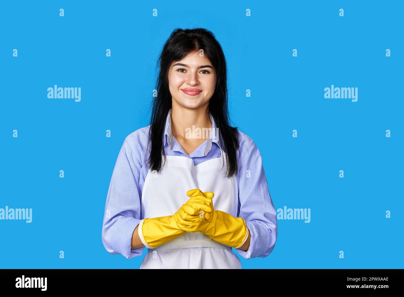 femme caucasienne en gants de caoutchouc jaune et tablier plus propre isolé sur fond bleu. nettoyage Banque D'Images