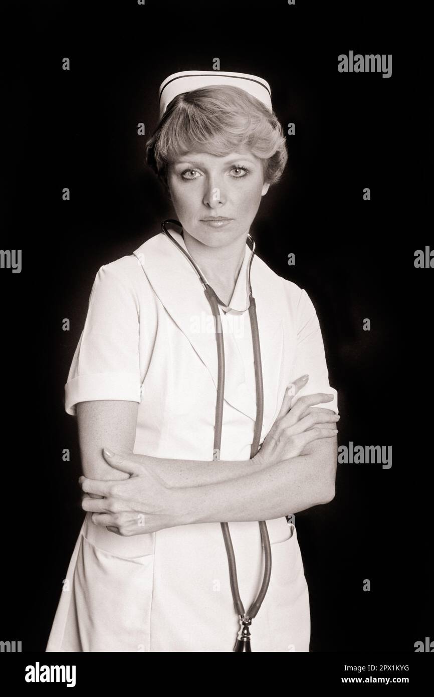 1970S INFIRMIÈRE BLONDE PORTRAIT PORTANT UNE CASQUETTE ET DES BRAS DE STÉTHOSCOPE CROISÉS À LA TAILLE GRAVE INTÉRESSÉ EXPRESSION REGARDANT LA CAMÉRA - N2499 HAR001 SARS CONFIANCE STÉTHOSCOPE B&W CONCERNÉ CONTACT OCULAIRE PROFESSIONNELS DE LA SANTÉ PROFESSIONNELS PROFESSIONNELS DE LA GUÉRISON ET DE LA SANTÉ PROFESSIONNELS GUÉRISSEURS PRATICIENS SOUTIEN SINCÈRE SOLENNEL FOCALISÉ INTENSE MOYENNE-ADULTE PROFESSIONNEL DE LA TAILLE JEUNE FEMME ADULTE NOIR ET BLANC ATTENTION RACE BLANCHE HAR001 INTENTION DÉMODÉE Banque D'Images