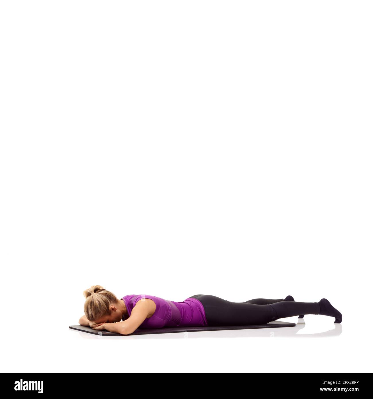 Préparation mentalement pour un entraînement. Une jeune femme couché face vers le bas sur son tapis d'exercice et renforçant ses fessiers. Banque D'Images