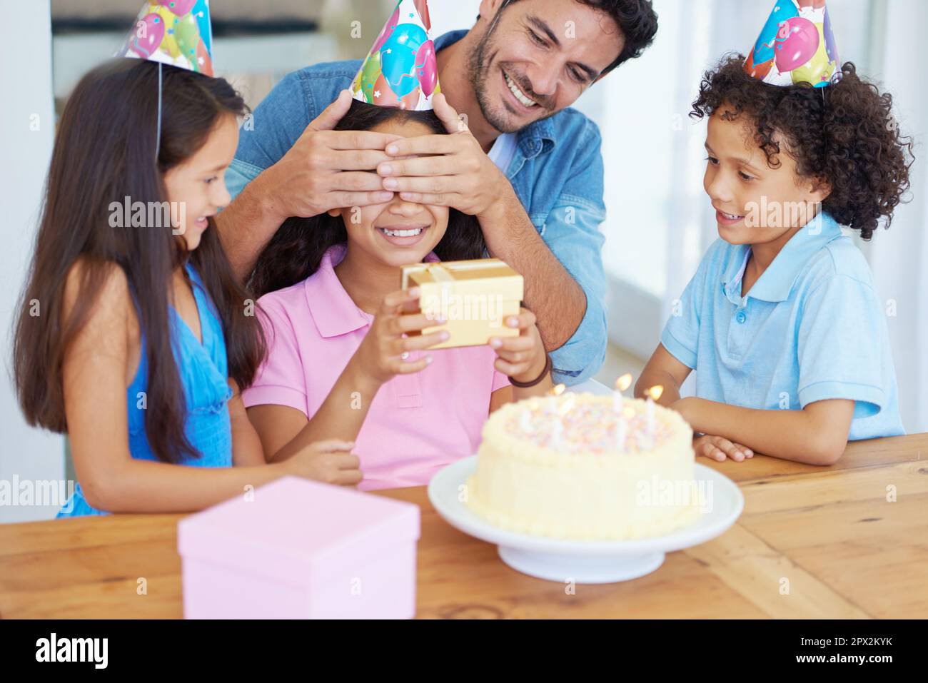 Devinez ce qu'il est. un père couvrant les yeux de ses filles à sa fête d'anniversaire. Banque D'Images