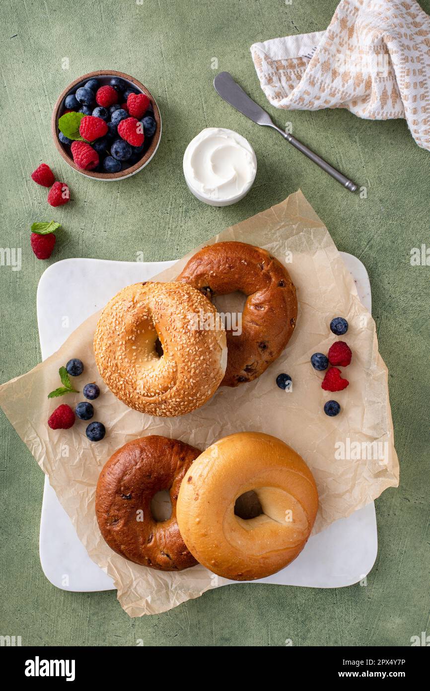 Bagels maison fraîchement cuits sur un papier parchemin prêt à manger, raisins secs de cannelle, sésame et bagel simple servi avec du fromage à la crème et des baies fraîches Banque D'Images